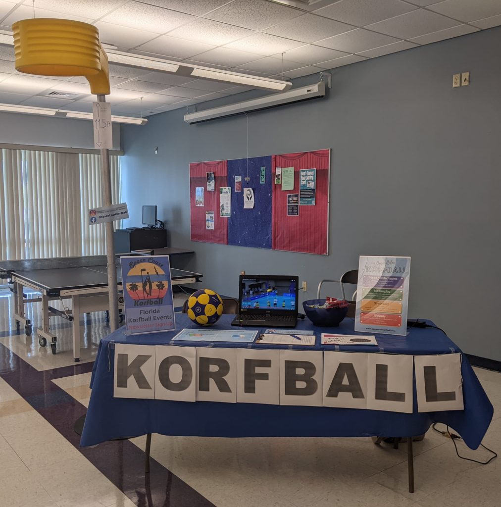 A korfball basket standing indoors next to a table that's set up to demonstrate Korfball.